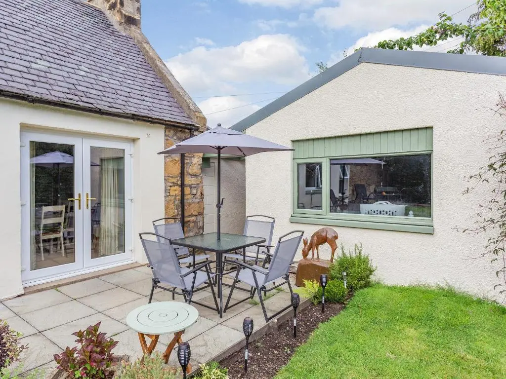 a patio with a table with chairs and an umbrella at Holly Tree Cottage in Tain