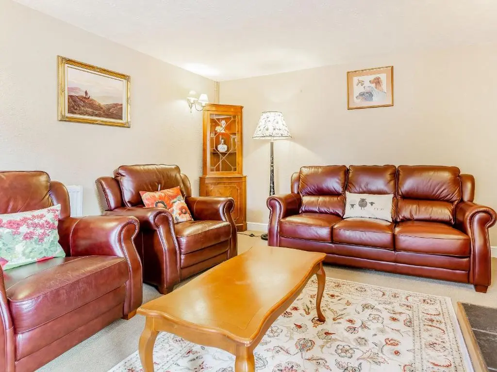 a living room with leather furniture and a table at Holly Tree Cottage in Tain