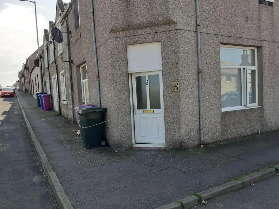 a building with a white door and a trash can at Lossiemouth Seaside Flat in Lossiemouth