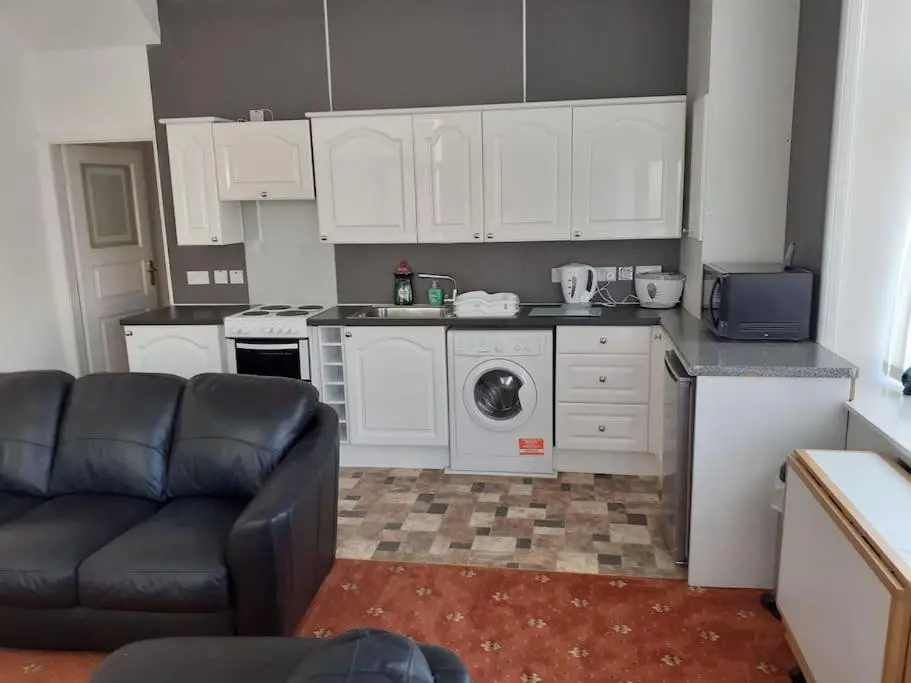 a kitchen with white cabinets and a black couch at Lossiemouth Seaside Flat in Lossiemouth