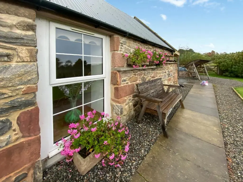a stone house with a bench and flowers on a patio at Paterson Cottage in Tore