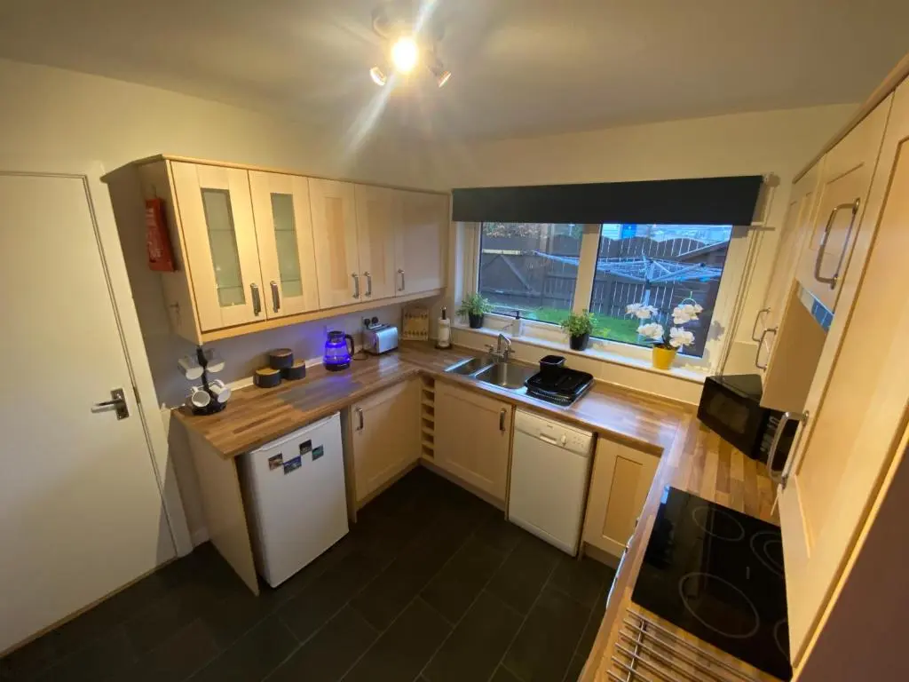 a small kitchen with wooden cabinets and a window at Delightful, central 3 bedroom house with garden & free parking in Inverness