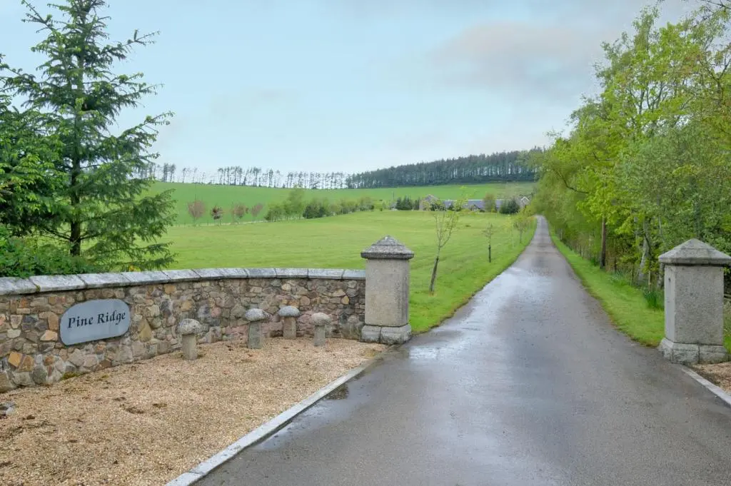 a road with a stone wall next to a field at Stunning Country House - Cinema, Games Room & Hot Tub in Inverurie