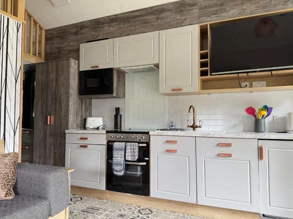 a kitchen with white cabinets and a black oven at The Smolt Pod - Beautiful, luxury pod in Aberlour
