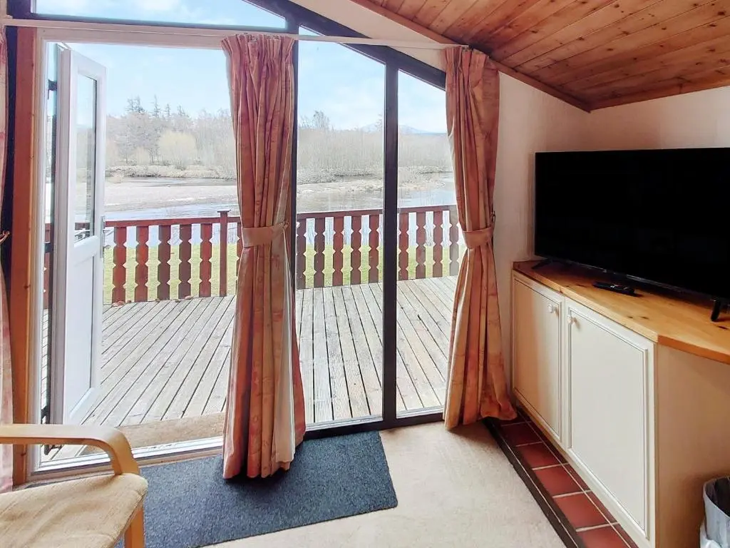 a living room with a television and a screened in porch at 27 Aviemore Holiday Park in Aviemore