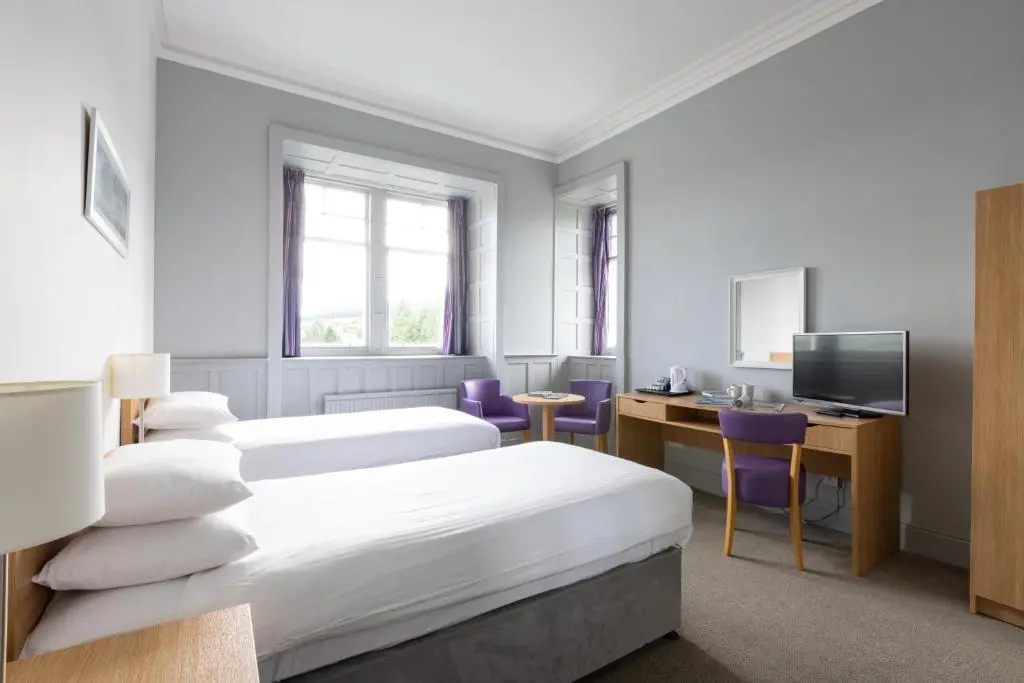 a hotel room with two beds and a desk at The Highland Hotel by Compass Hospitality in Strathpeffer