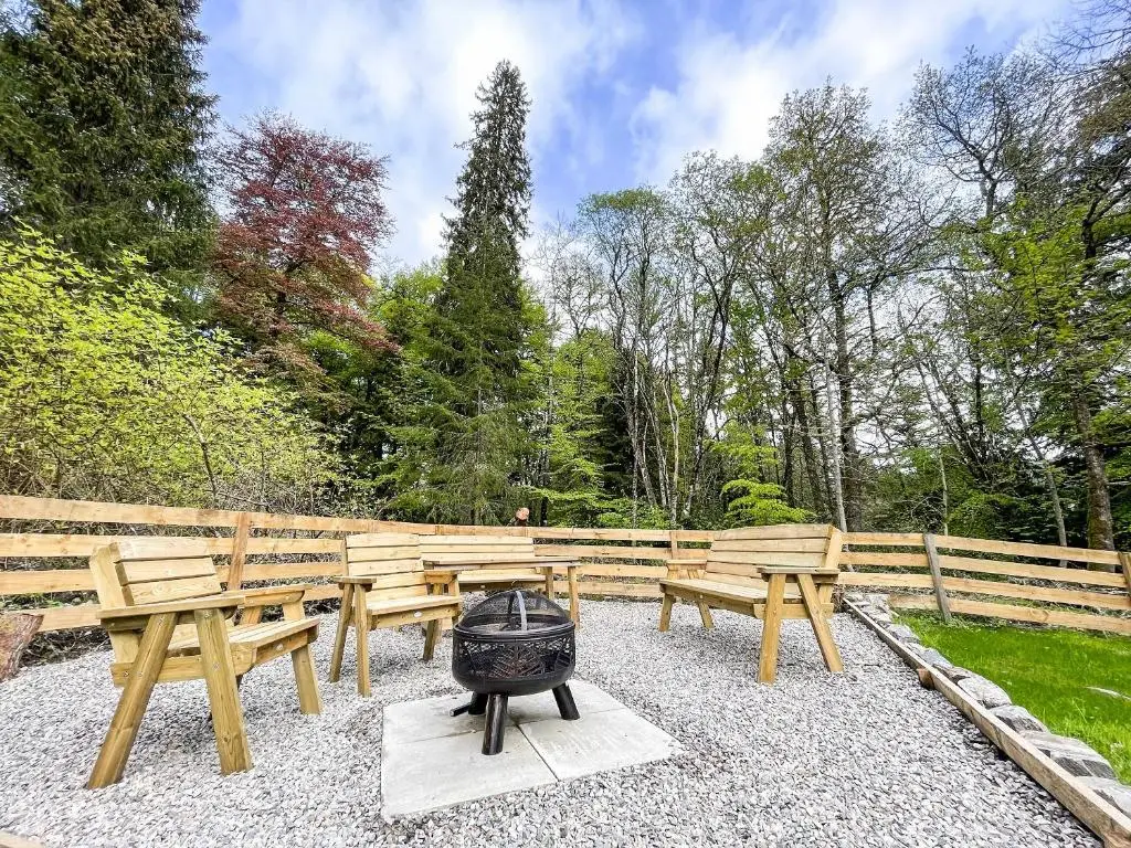 a fire pit with wooden benches and a grill at East Lodge in Contin