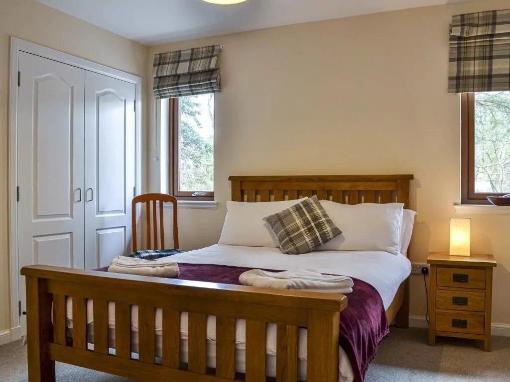 a bedroom with a wooden bed and two windows at Golf View in Aboyne