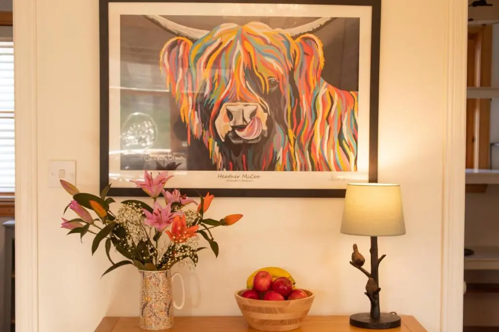 a painting of a cow on a wall with a vase of fruit at Longfield, Daviot in Inverness