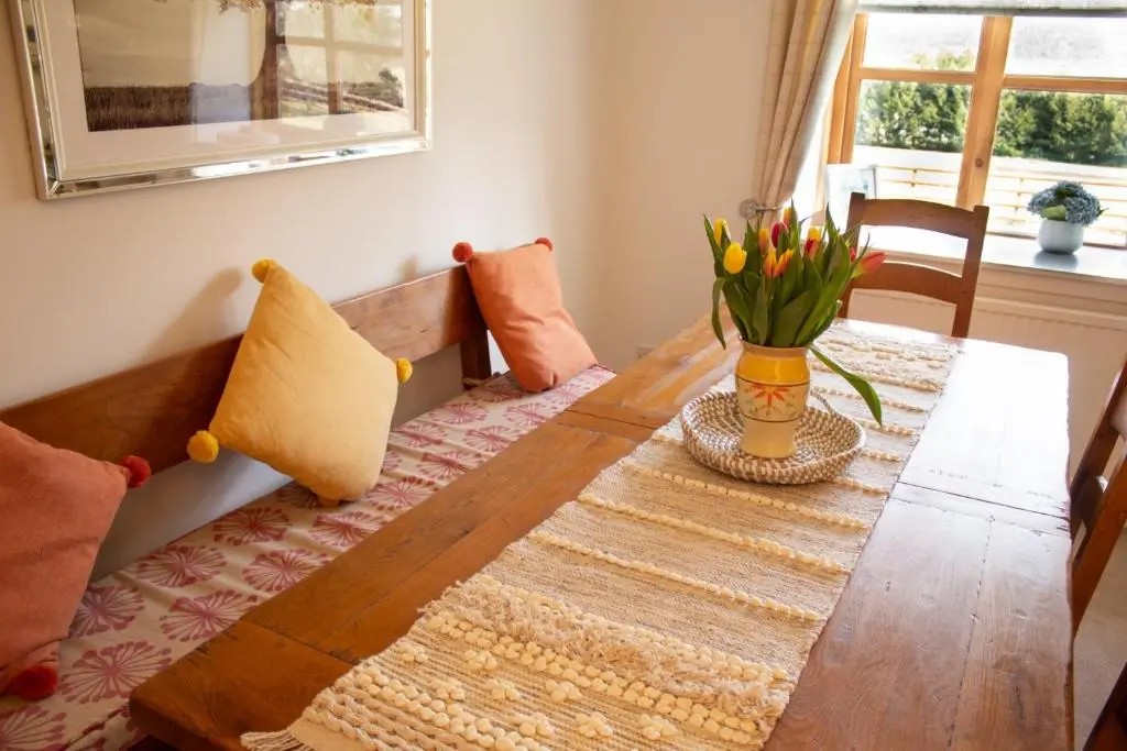 a dining room table with a vase of flowers on it at Longfield, Daviot in Inverness