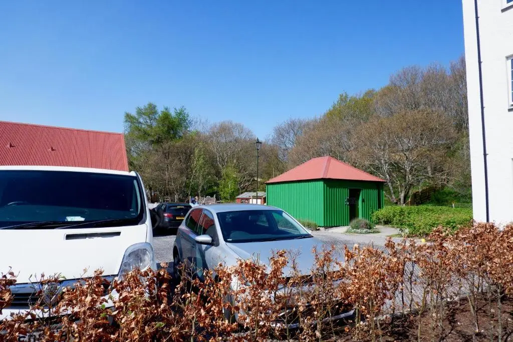 a car parked in a parking lot with a green building at No 7 Quiet, two bedroom Ground Floor Flat in Tornagrain Great for early Airport departures or late flights in Dalcross