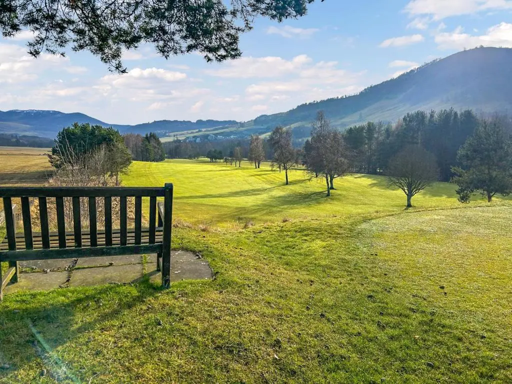 a park bench sitting in a field of grass at Riverside Cottage in Blair Atholl