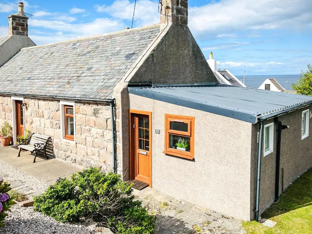 a small stone house with an orange door and windows at Portknockie Escape in Portknockie