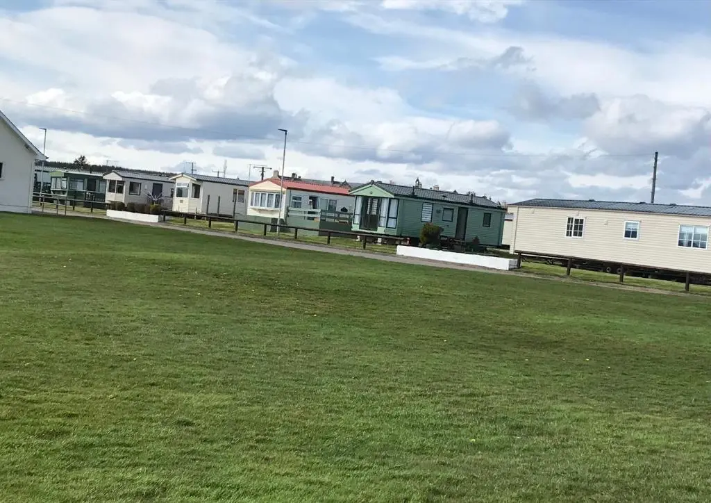 a row of houses in a field with a grass field at Melody Brooks Caravan Park in Portknockie
