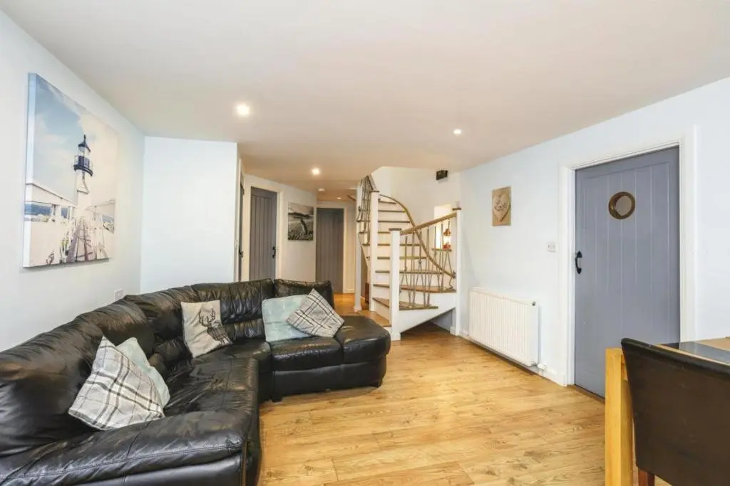 a living room with a black leather couch and a staircase at 29 Seafield Street in Whitehills