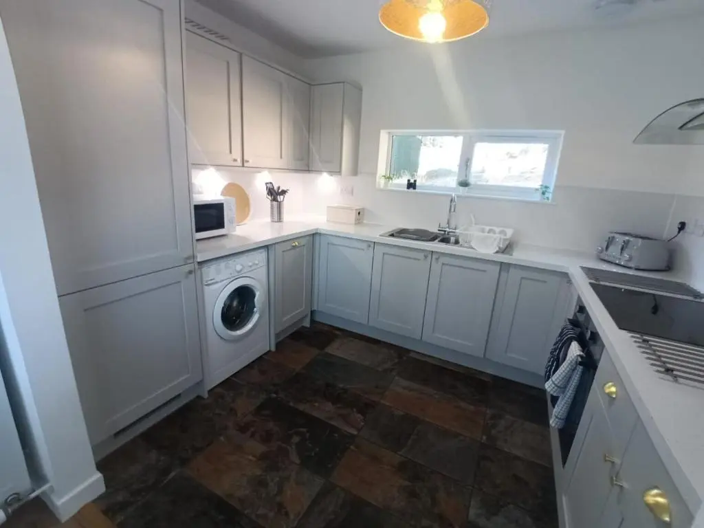 a kitchen with white cabinets and a washing machine at Sawmill Cottage in Grantown on Spey