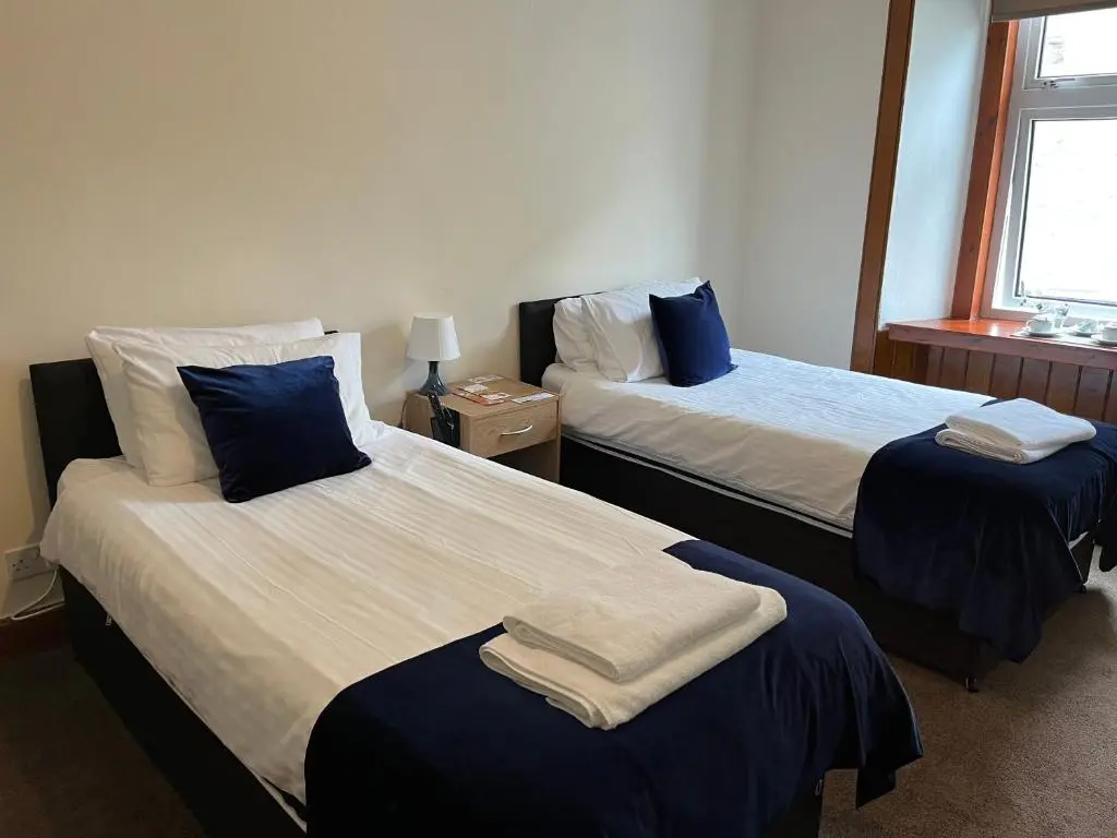 a bedroom with two beds with blue and white sheets at Caithness Inn in Wick