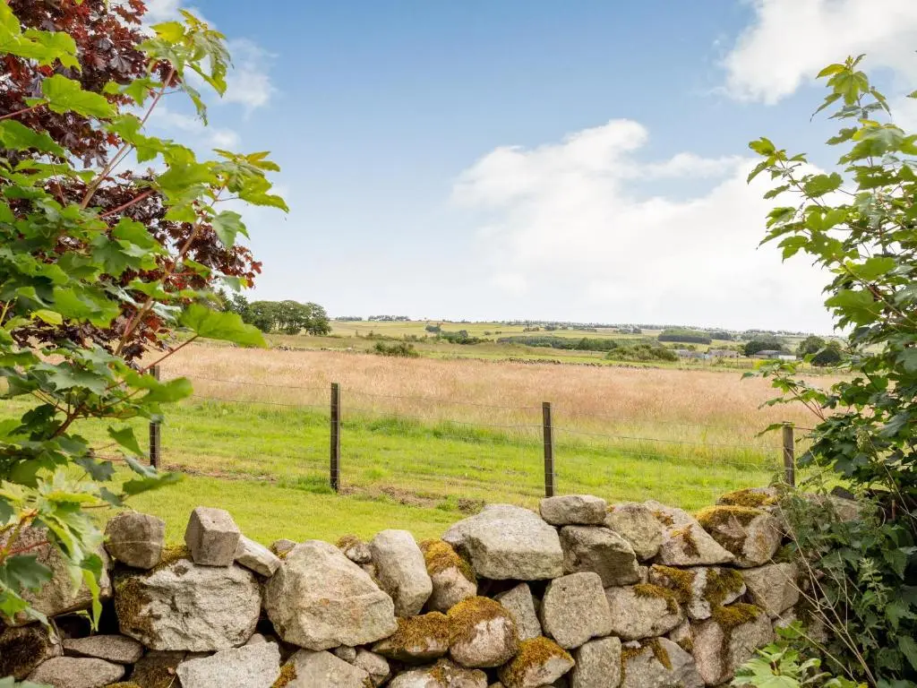 a stone wall with a field in the background at Glen Nevis Cottage in Port Elphinstone