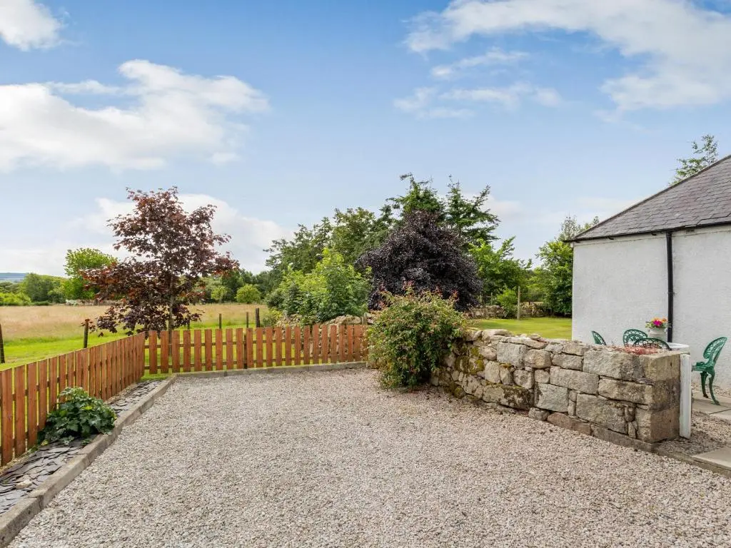 a wooden fence and a stone wall next to a house at Glen Nevis Cottage in Port Elphinstone