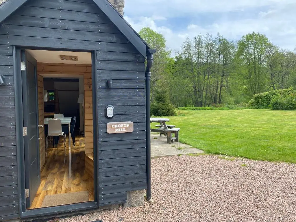 a black shed with a table and a bench in a yard at Crofts Mill in Ballater