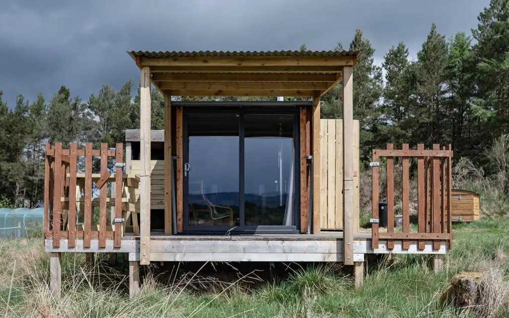 a small wooden house with two chairs in a field at Highland Shepherd Huts in Nethy Bridge