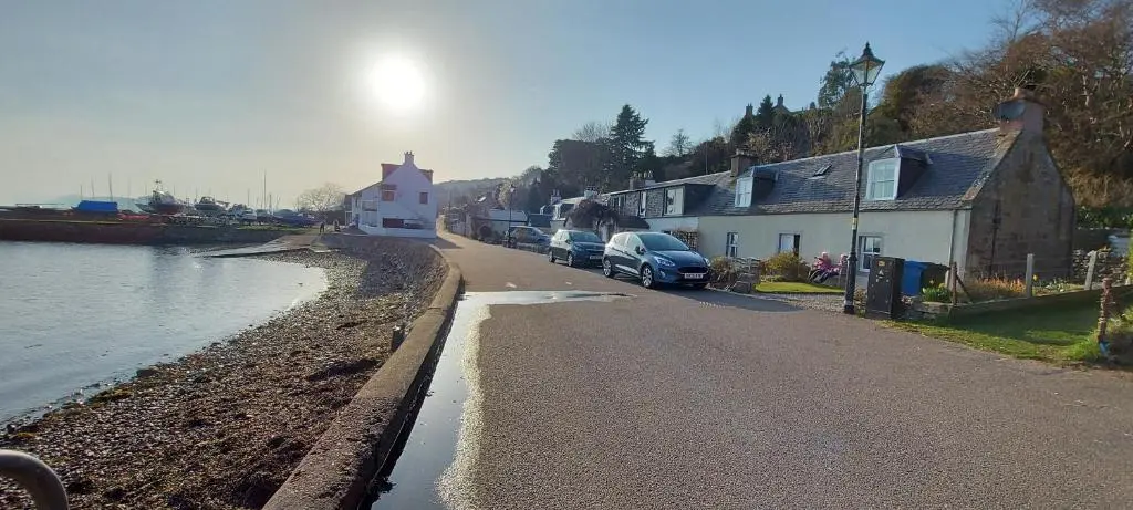 a street with cars parked on the side of a river at Clematis Cottage, Fortrose in Fortrose