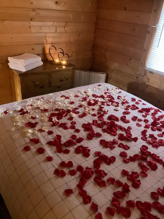 a bed covered with red rose petals on it at Log Cabin in the City with hot tub in Culloden