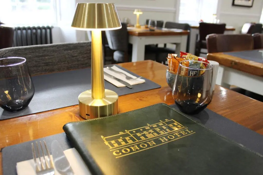 a book on a table with a lamp and glasses at Conon Hotel in Dingwall