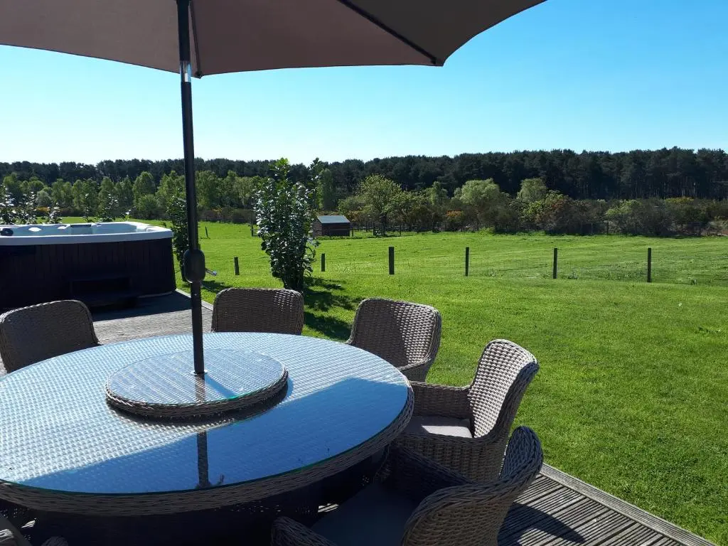 a table with chairs and an umbrella in a field at Clovenstone Lodges in Inverurie