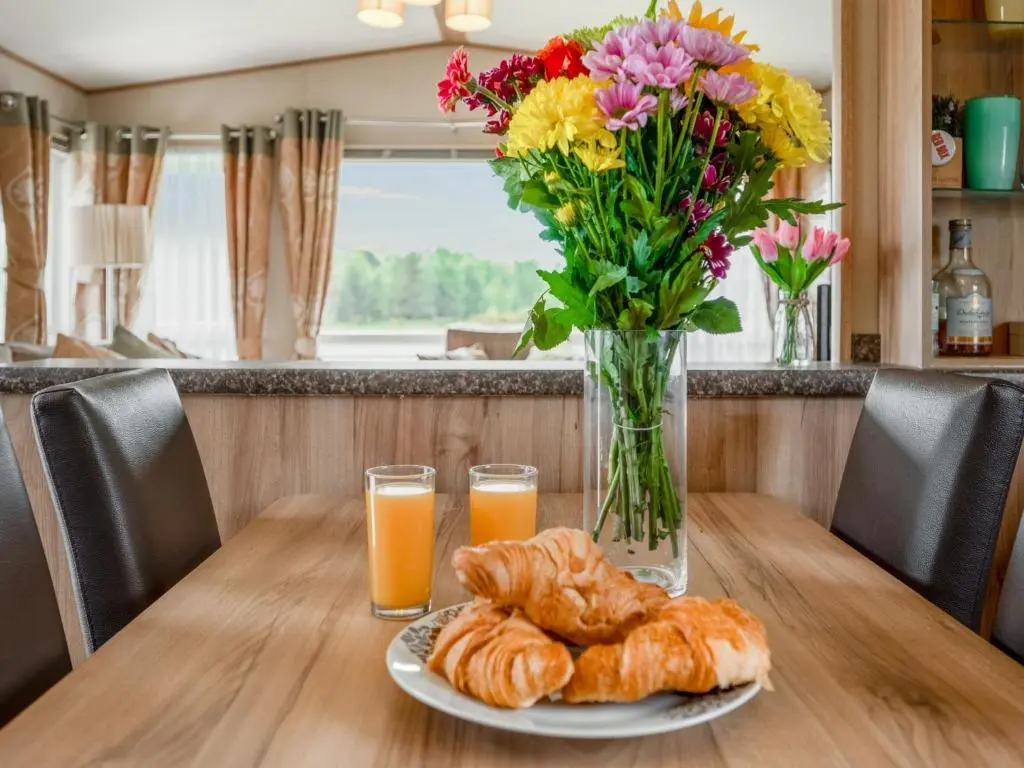 a table with a plate of croissants and flowers and orange juice at Holiday Home Golf View by Interhome in Nairn