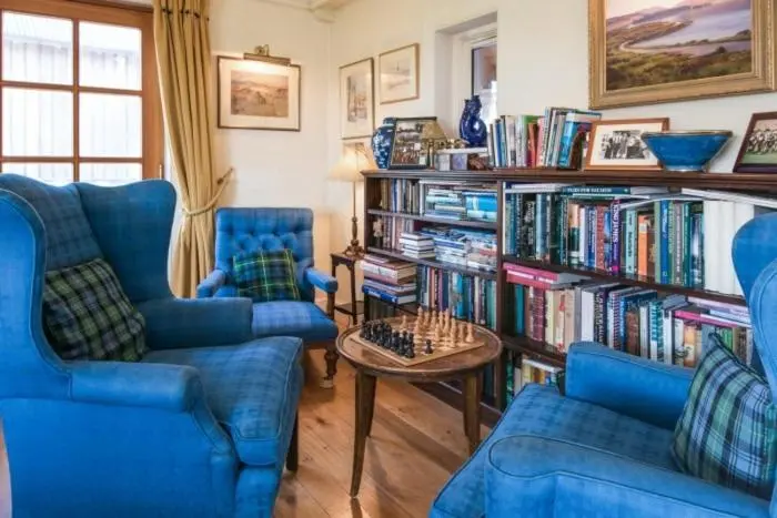 a living room with two blue chairs and a book shelf with books at Clashindeugle Farmhouse & Annex in Grantown on Spey