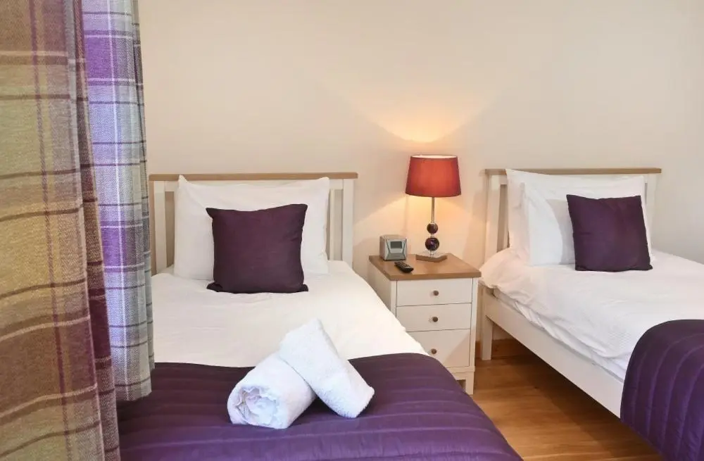 two beds in a room with purple and white pillows at Inverness City Apartment in Inverness