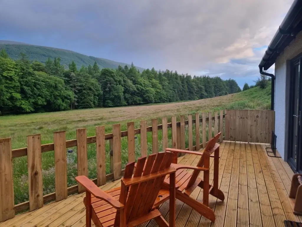 two wooden chairs sitting on a deck with a view at Cozy Nook in Spean Bridge