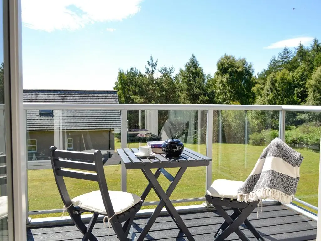 a patio table and chairs on a deck with a view of a yard at Queen's View Lodge in Inchmarlo