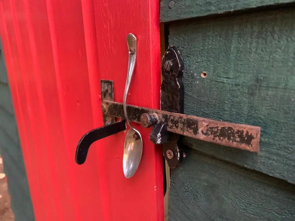 a rusty door latch on a red door at Birkenshaw - Beautiful Shepherd\u2019s Hut in the Highlands. in Dornoch
