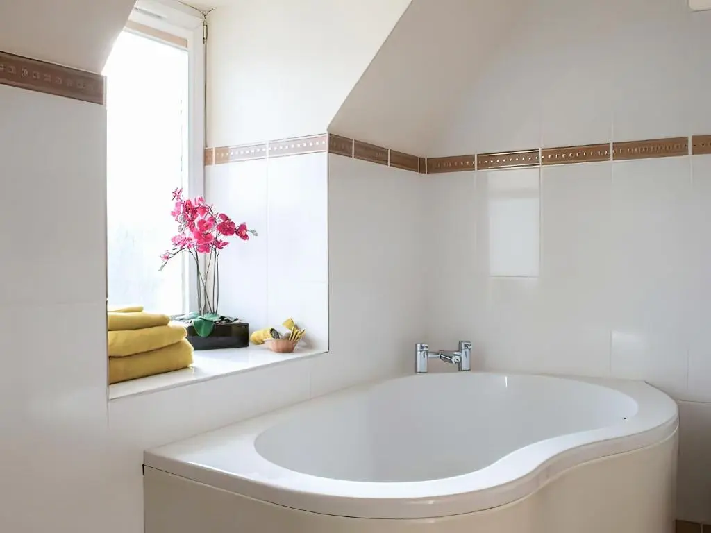 a white bathroom with a tub and a window at Hill Cottage in Ardmair