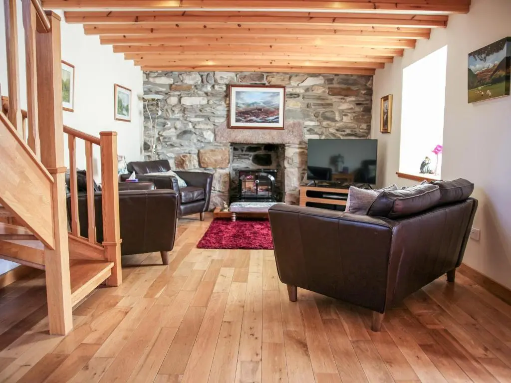 a living room with couches and a stone fireplace at Hill Cottage in Ardmair