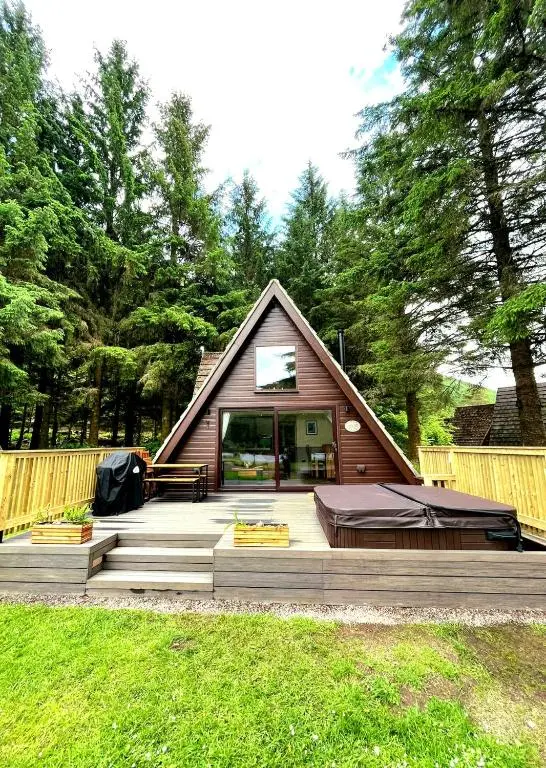 a small house with a porch and a deck at Bonnie Lodge-Lochside Location with Hot Tub in Invergarry