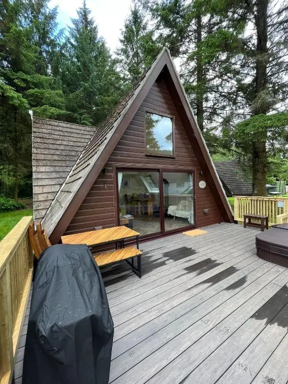 a cabin with a wooden deck with a bench on it at Bonnie Lodge-Lochside Location with Hot Tub in Invergarry