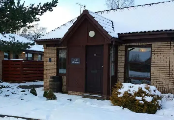 a house with a brown door in the snow at Aviemore Glenlivet Lodge in Aviemore