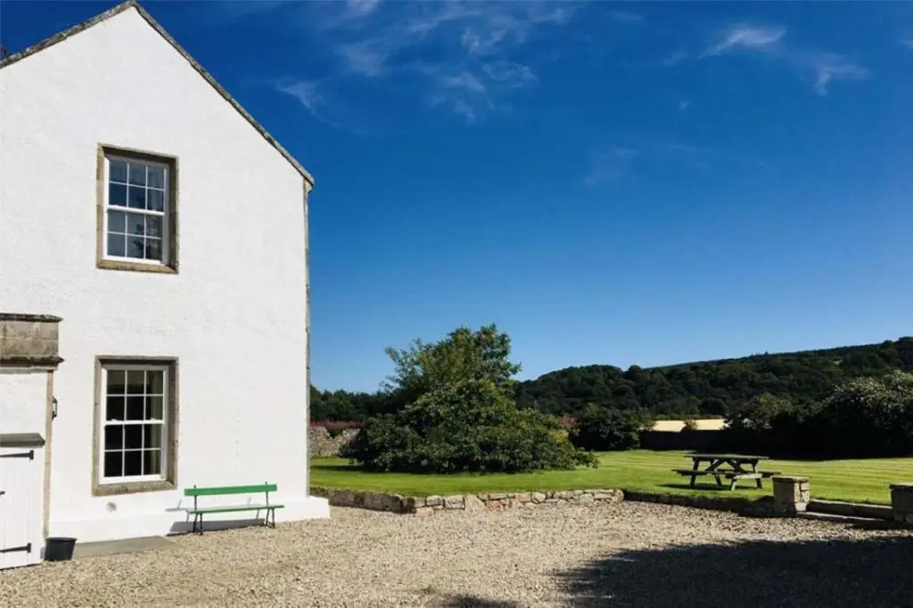 a white building with a green bench next to a field at Garbity Farmhouse - beautiful 6-bedroom Farmhouse with open fires in Fochabers