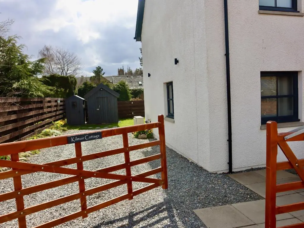 a red fence next to a white building at Kilmuir Cottage in Tomintoul