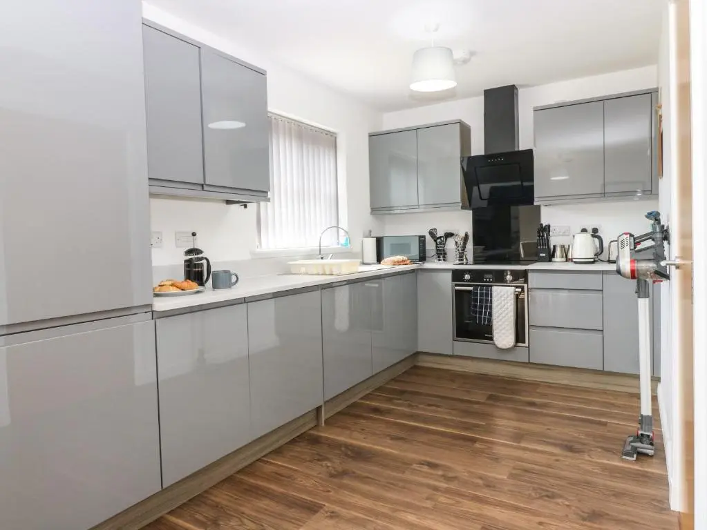 a kitchen with white cabinets and a wooden floor at Kilmuir Cottage in Tomintoul
