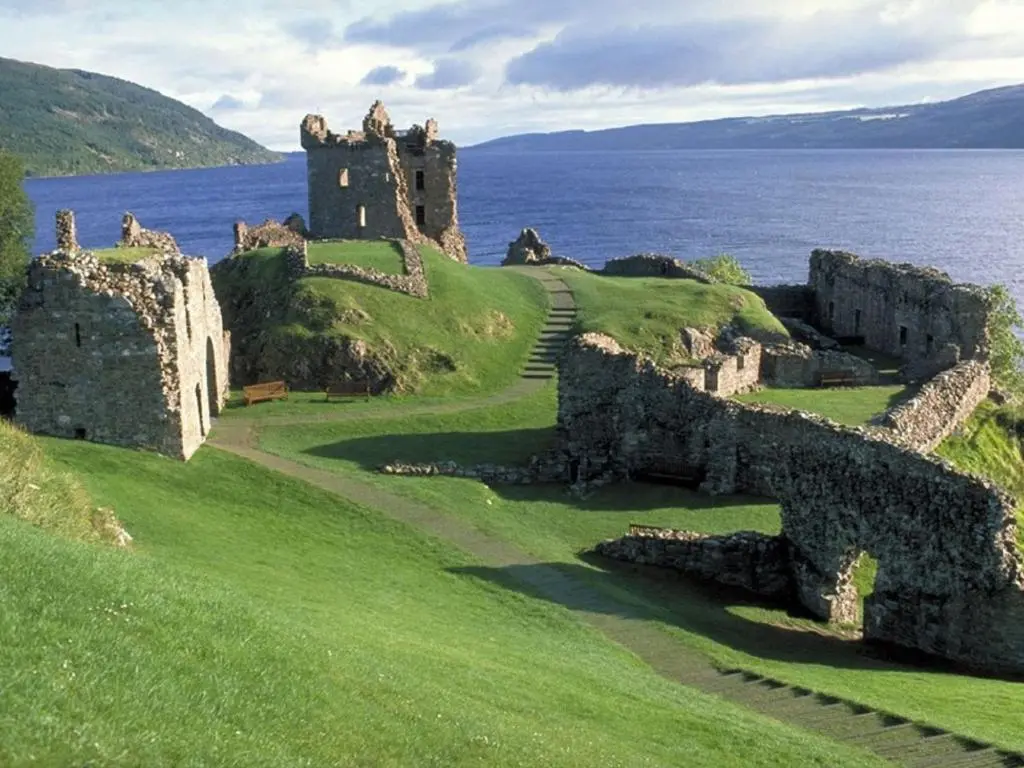 an old castle on a hill next to the water at Divach Lodge at Lochletter Lodges in Drumnadrochit