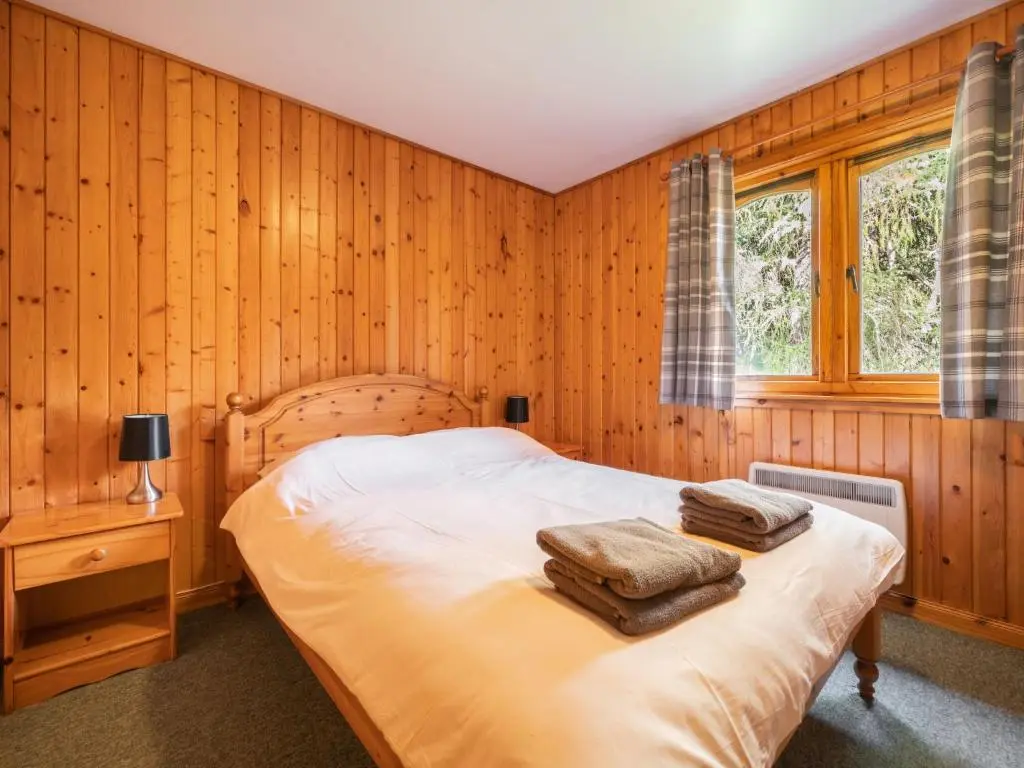 a bedroom with wooden walls and a bed with towels on it at Guisachan Lodge at Lochletter Lodges in Drumnadrochit
