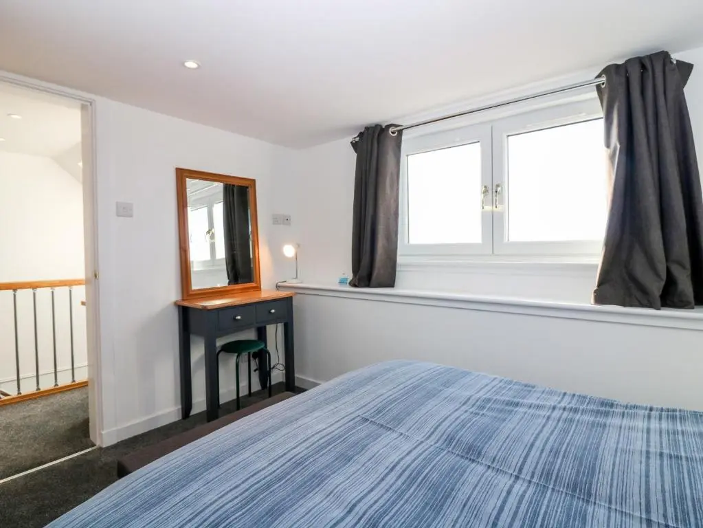 a bedroom with a bed and a desk and window at Dolphin Cottage in Banff