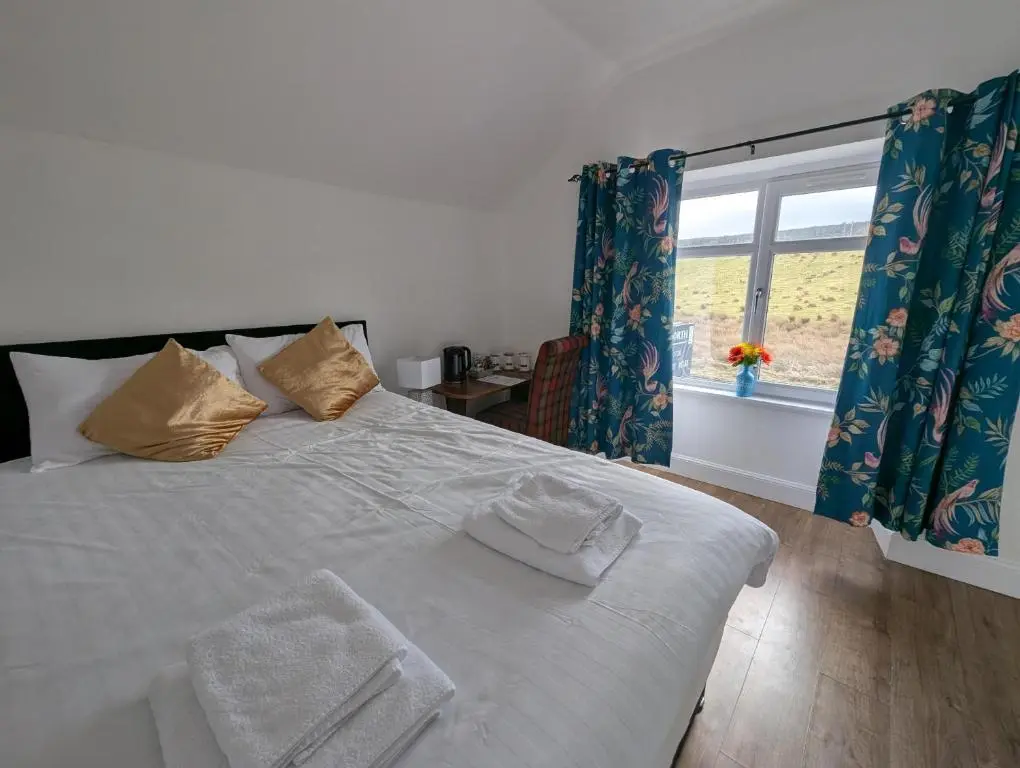 a bedroom with a white bed with blue curtains and a window at Old North Inn Hotel in Kirkhill