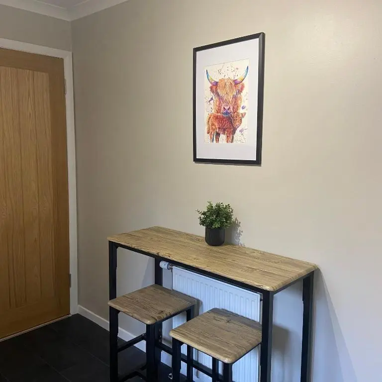 a table with two stools and a picture of a cow at Cathwill - Cosy 4 Star Cottage - Cairngorm National Park in Newtonmore