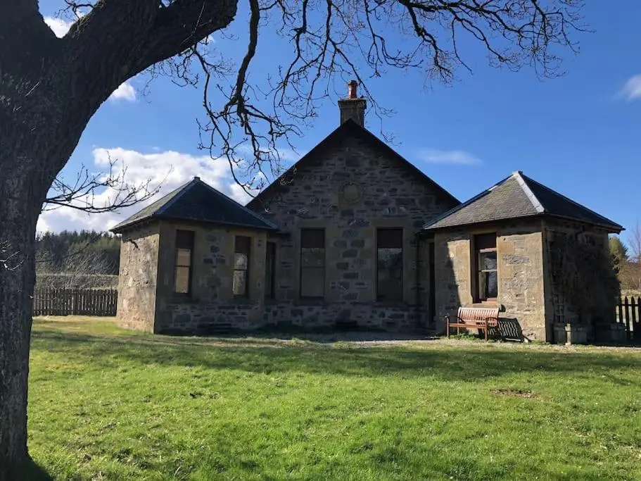 an old stone building in a field with a tree at *Cool, cosy cottage in the heart of the Highlands* in Kincraig