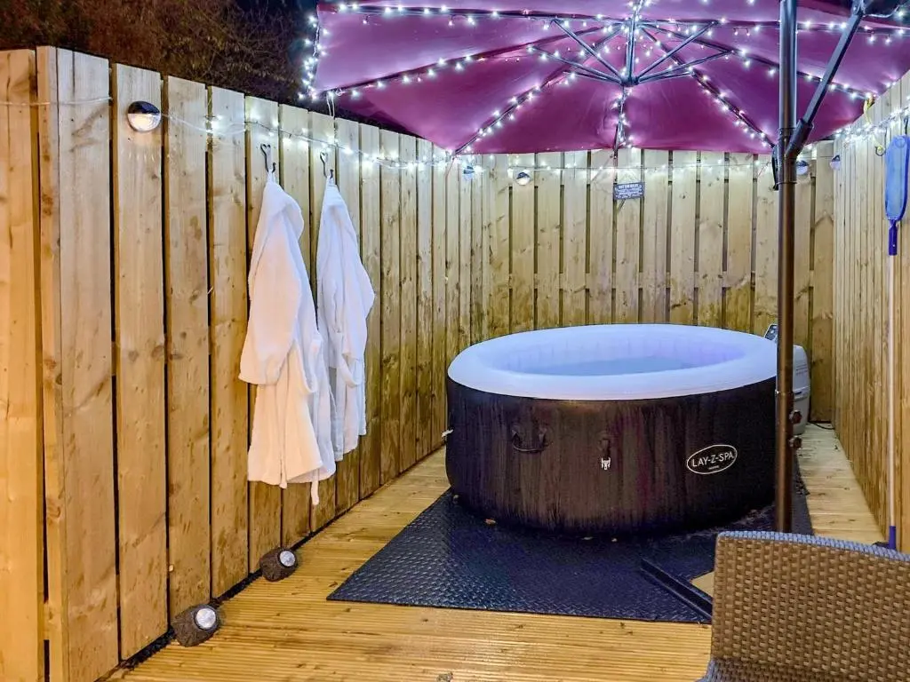 a wooden fence with a hot tub and an umbrella at The Dalmore Pod in Alness